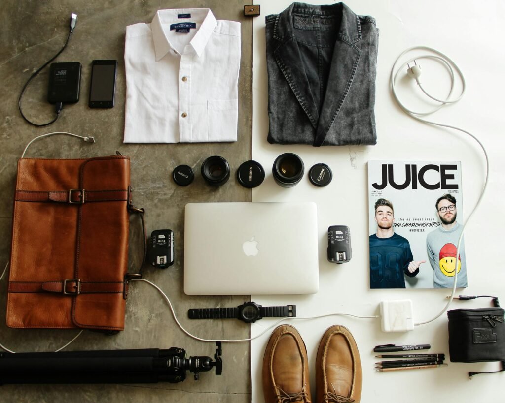 Neatly arranged travel essentials for men including clothing, tech gear, and a magazine.